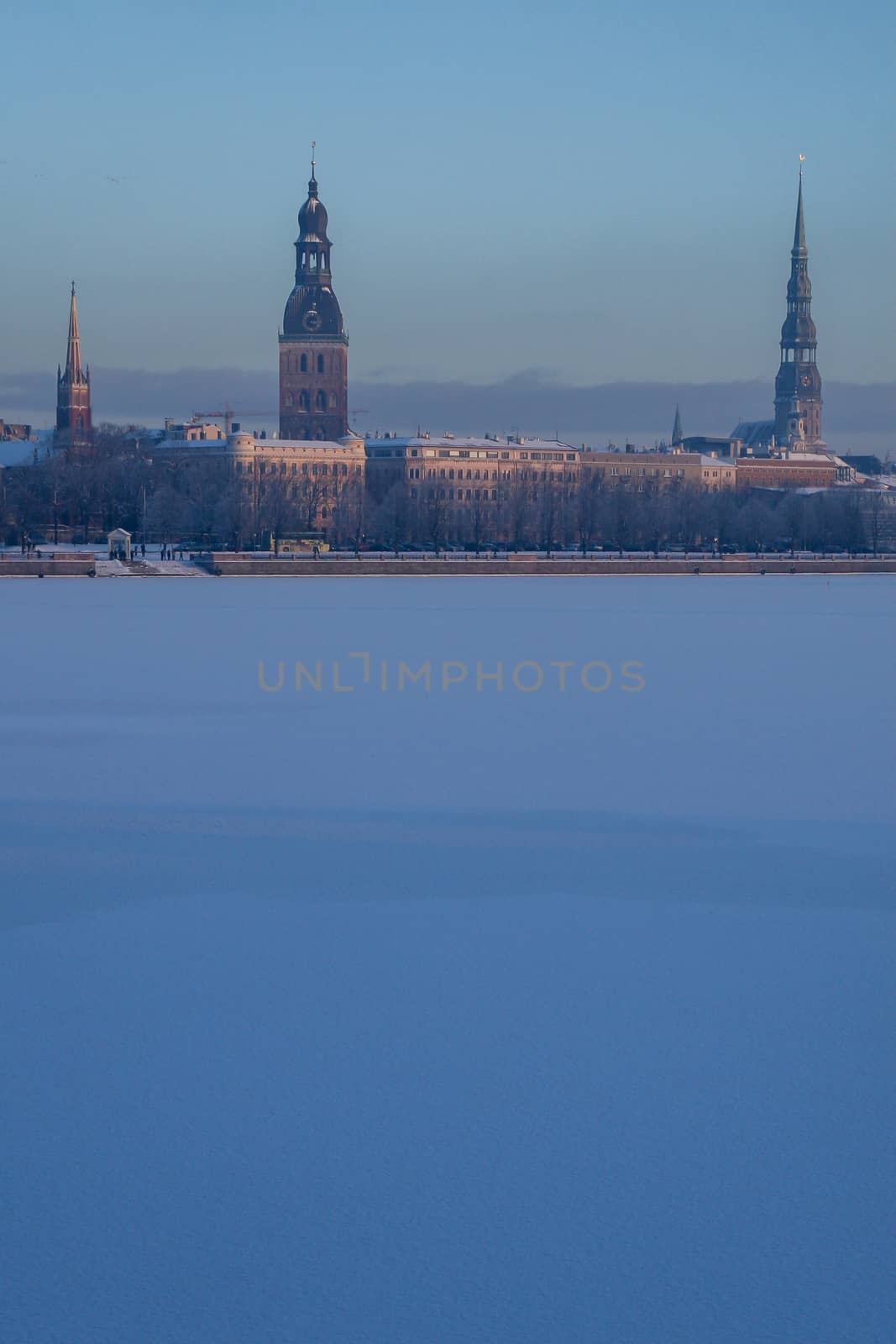 Riga view in winter; Riga, capital city of Latvia in winter time. View of St Peter's Church, St. Jacob's Cathedral and Anglican Church. View of Old Riga with frozen river Daugava in the foreground. City Riga with background of blue sky. 