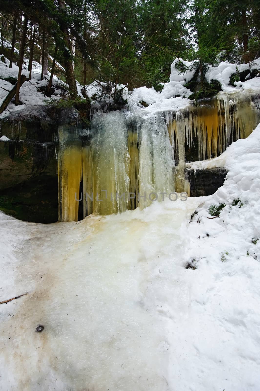 Frozen waterfalls on the rock, orange colored and snow