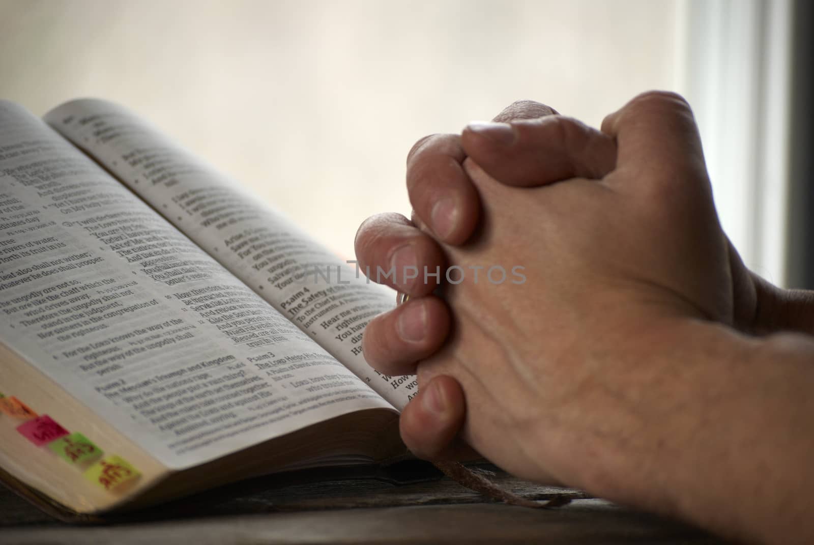 Man holding his hands close to the bible and praying.