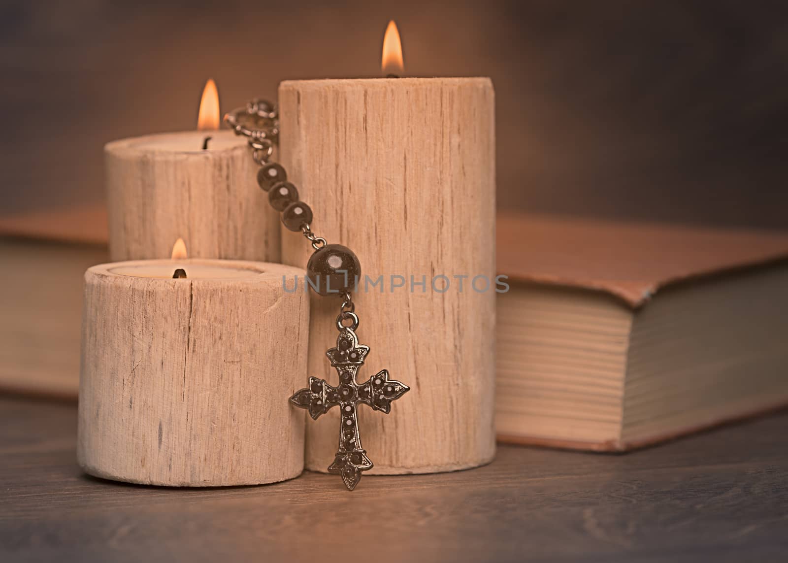 black rosary and crucifix resting on closed book near the candles on wooden table, religion school concept. Vintage style.