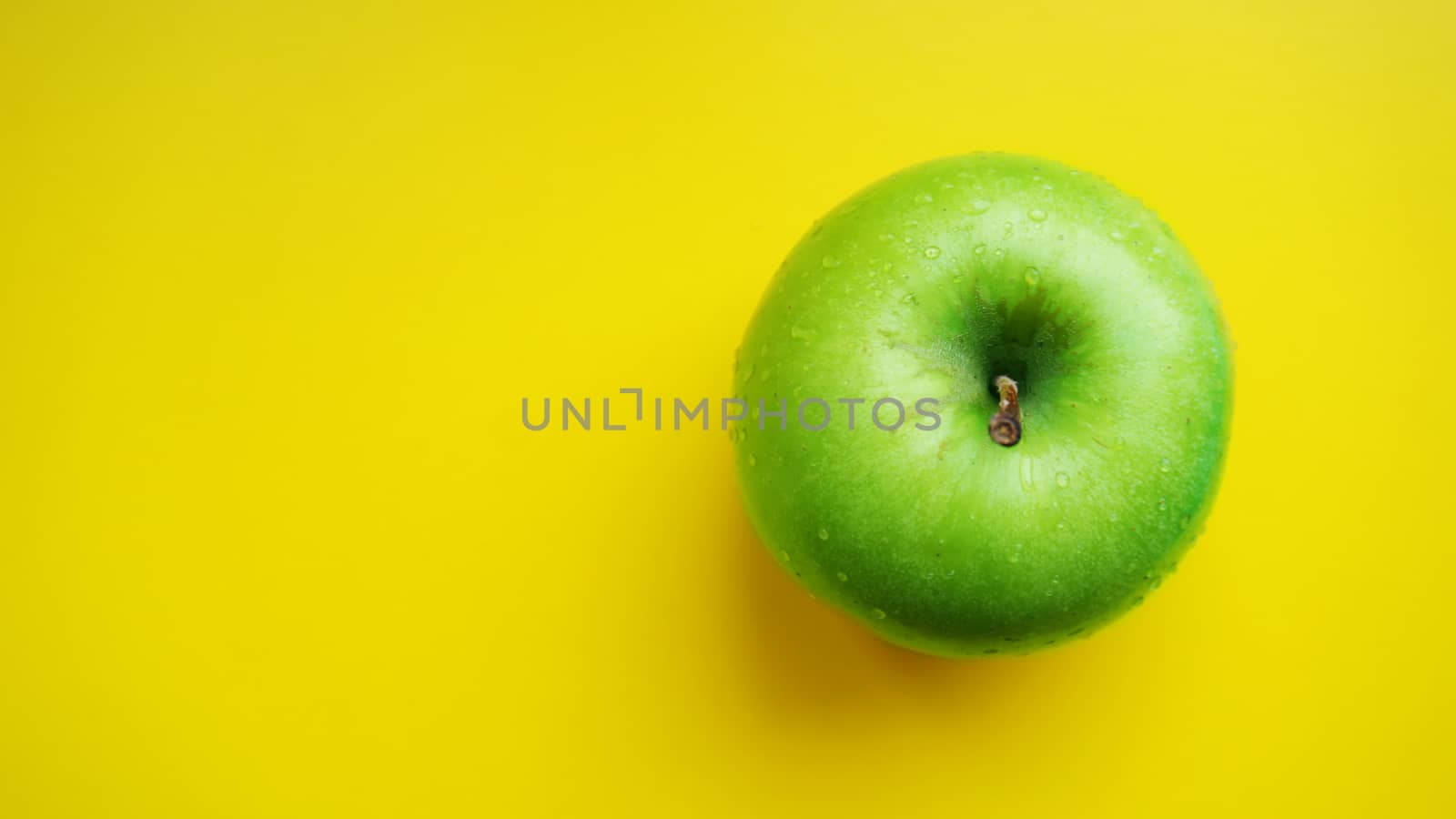 Green apple in water drops on yellow color background isolated close up macro top view