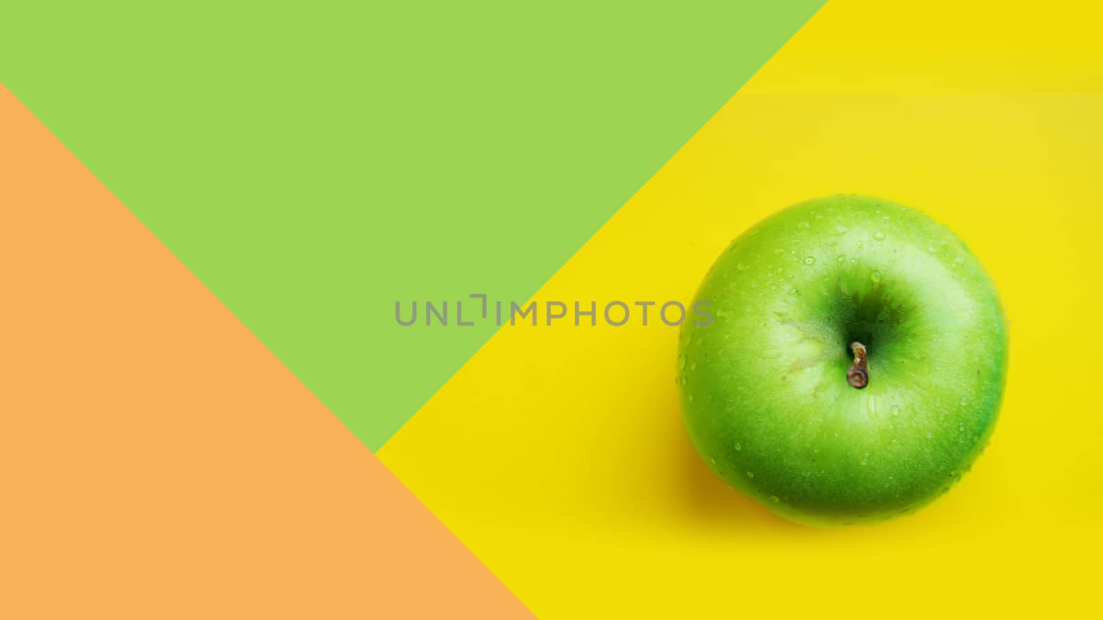 Green apple in water drops on yellow color background isolated close up macro top view