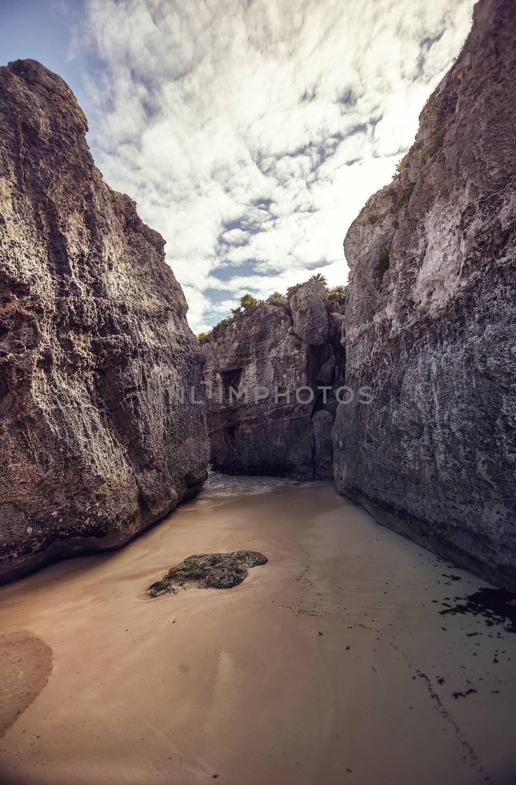 Rocky walls create a natural insenatira in the beach of the Tulum ruins in Mexico. Ertical shot. 