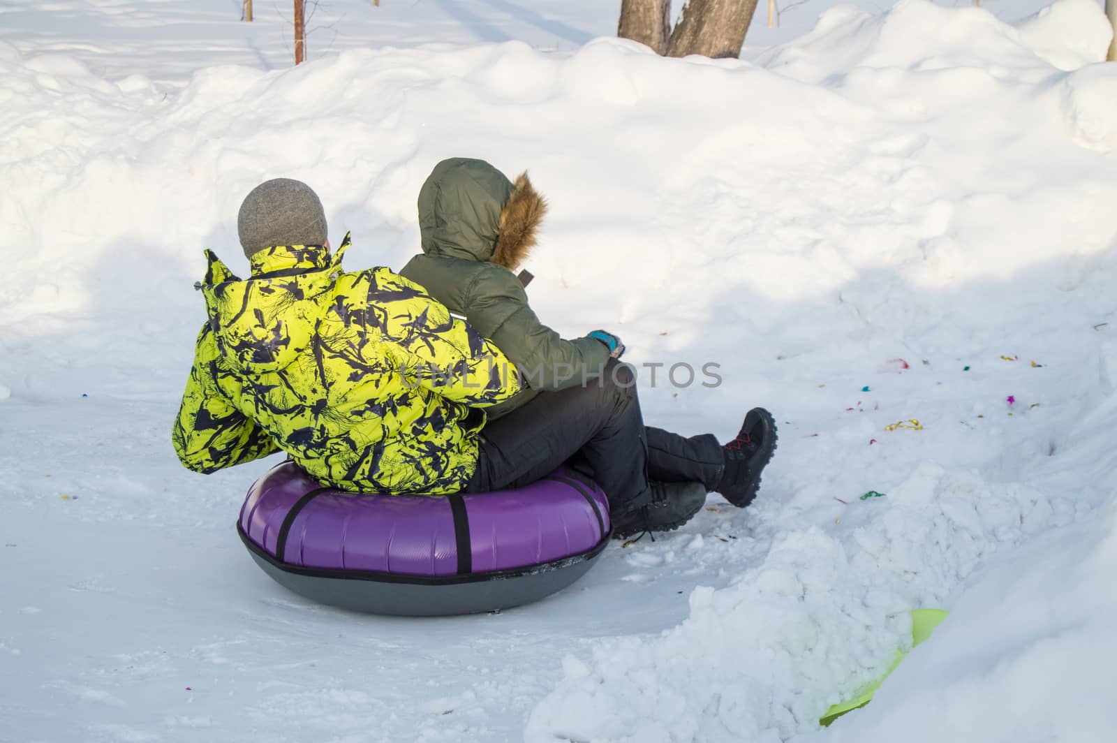 Winter entertainment. Two happy teenagers with pleasure ride on a tubing from the mountain. Sunny frosty day.