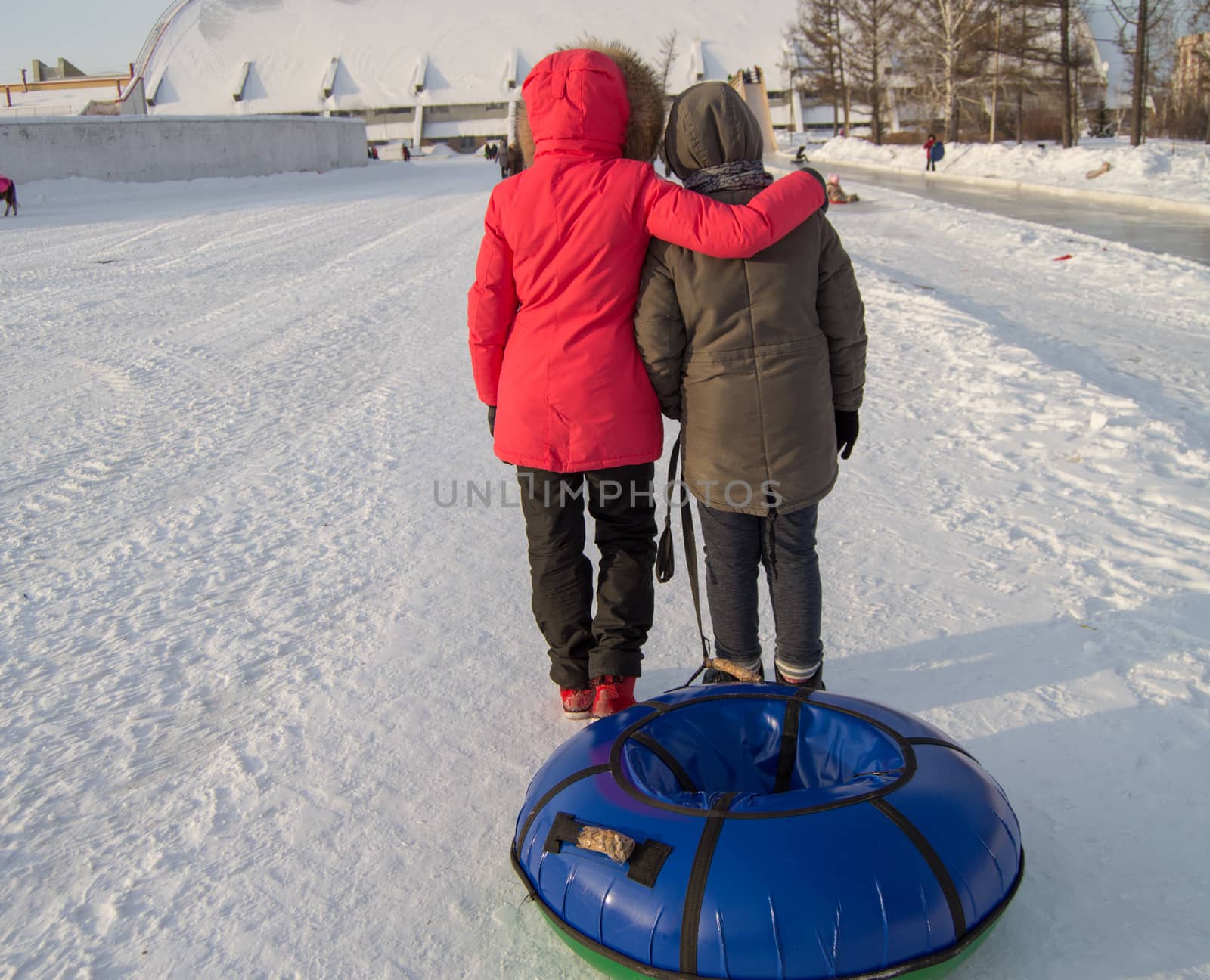 Two teen girls pull tubing after after sliding down the slope of an ice slide, winter fun in the Park.