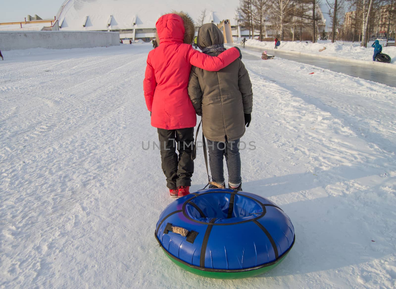 Two teen girls pull tubing after after sliding down the slope of an ice slide, winter fun in the Park.
