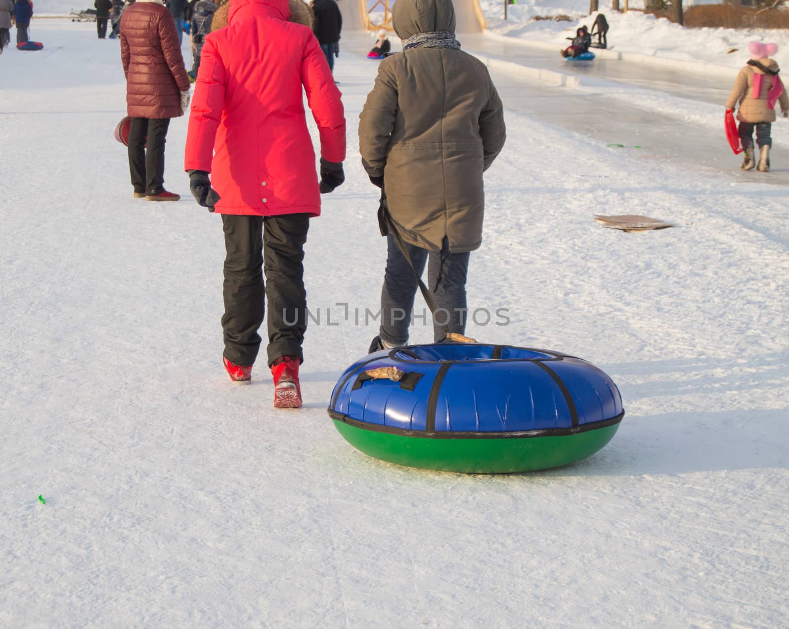 Two teen girls pull tubing after after sliding down the slope of an ice slide, winter fun in the Park by claire_lucia