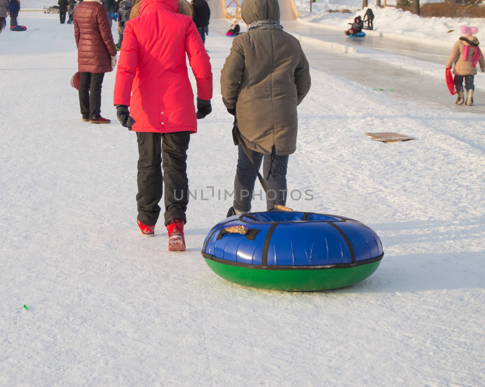 Two teen girls pull tubing after after sliding down the slope of an ice slide, winter fun in the Park.