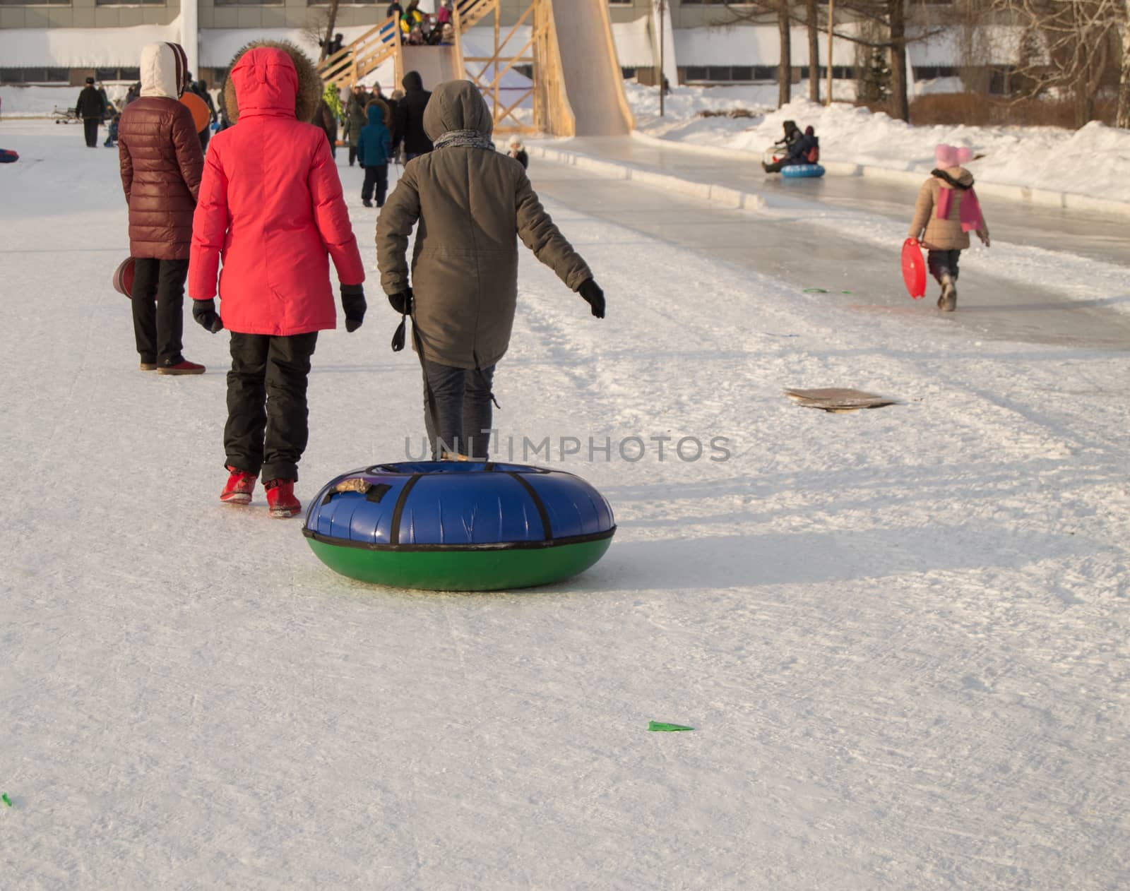 Two teen girls pull tubing after after sliding down the slope of an ice slide, winter fun in the Park.