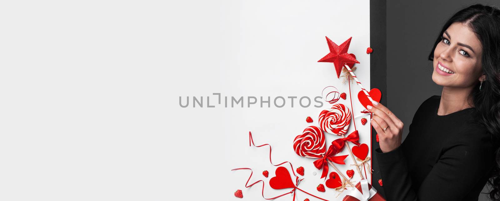 Beautiful woman with magic wand making valentines day decor of red hearts , ribbons, lollipops and strawberries , white copy space for text