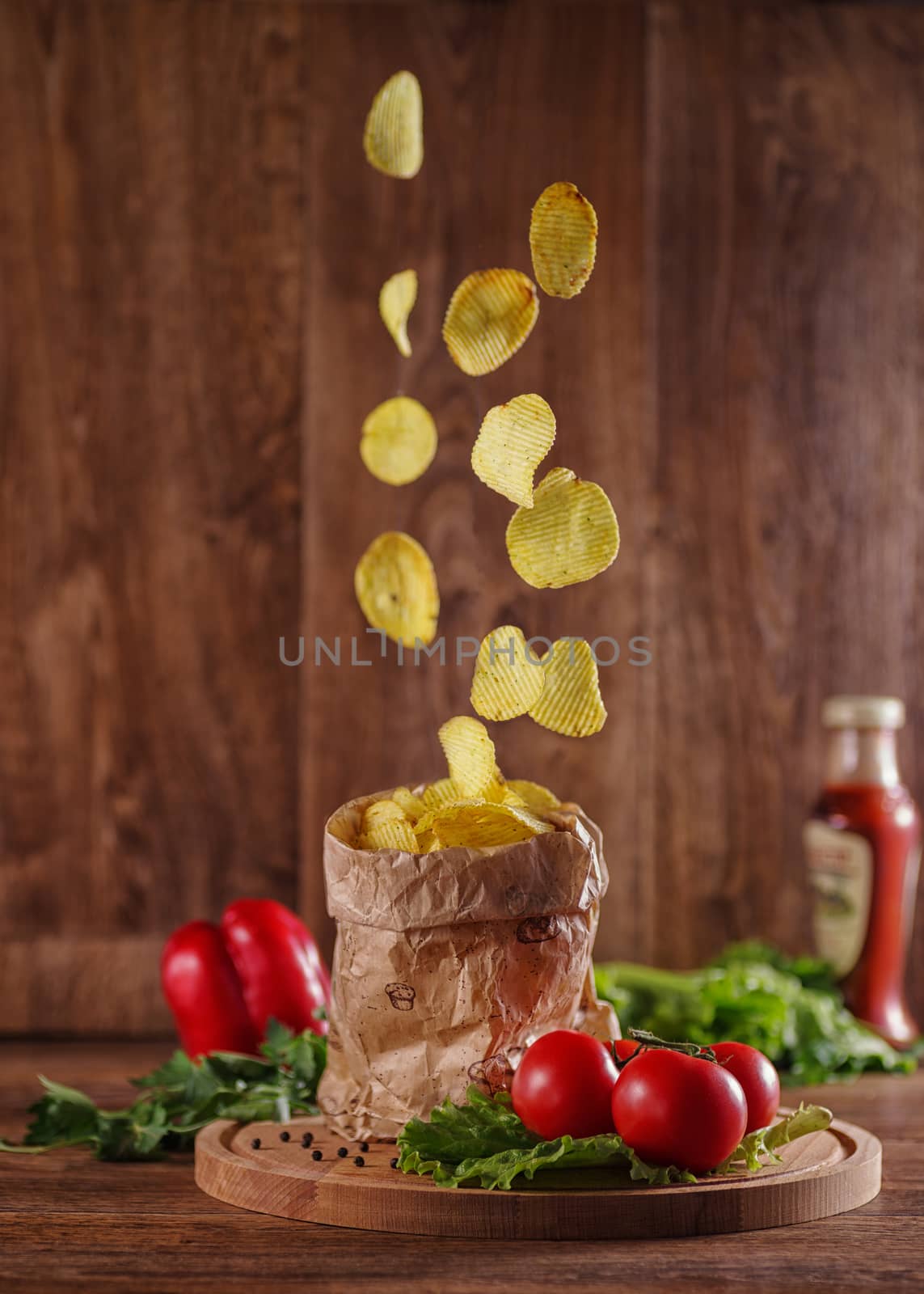 Potato chips falling into a paper bag on a rustic table.