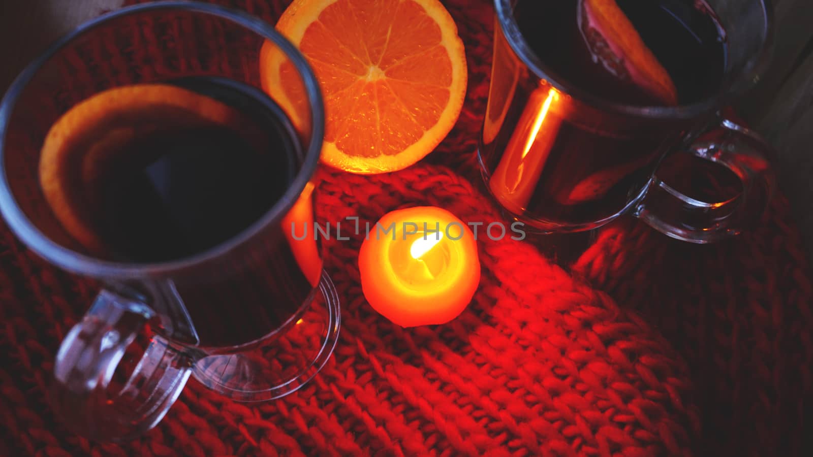 Mulled wine in glass mugs, burning candle on a dark red background. Red Hot wine with orange and red scarf