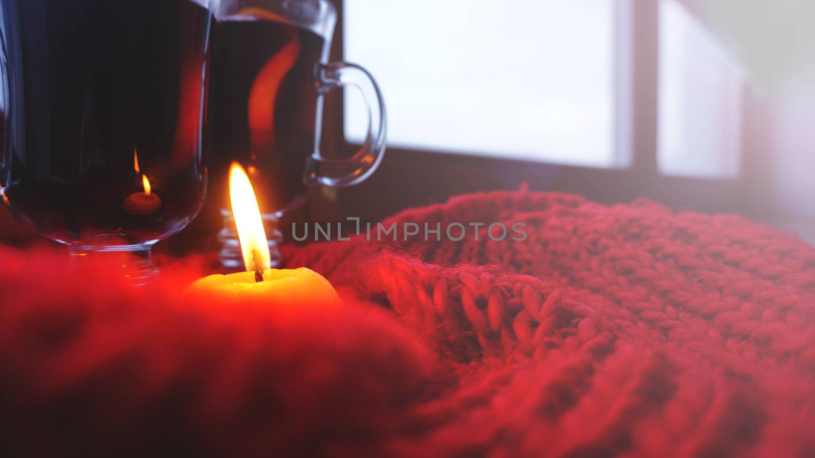 Mulled wine in glass mugs, burning candle on a dark red background. Red Hot wine with orange and red scarf