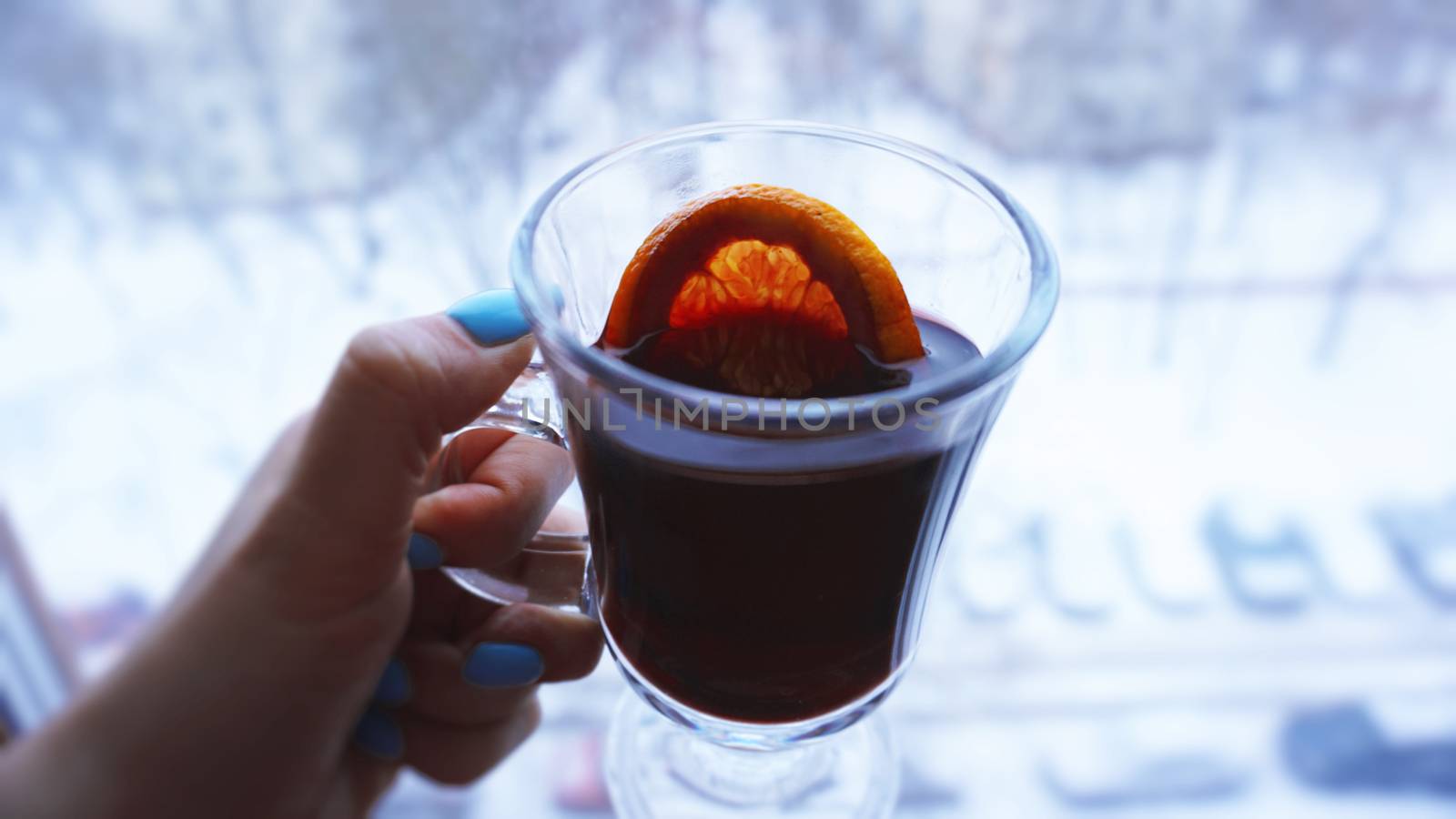 Woman holding mulled wine with spices and citrus fruit in her hand, close up in front of the window with a winter view