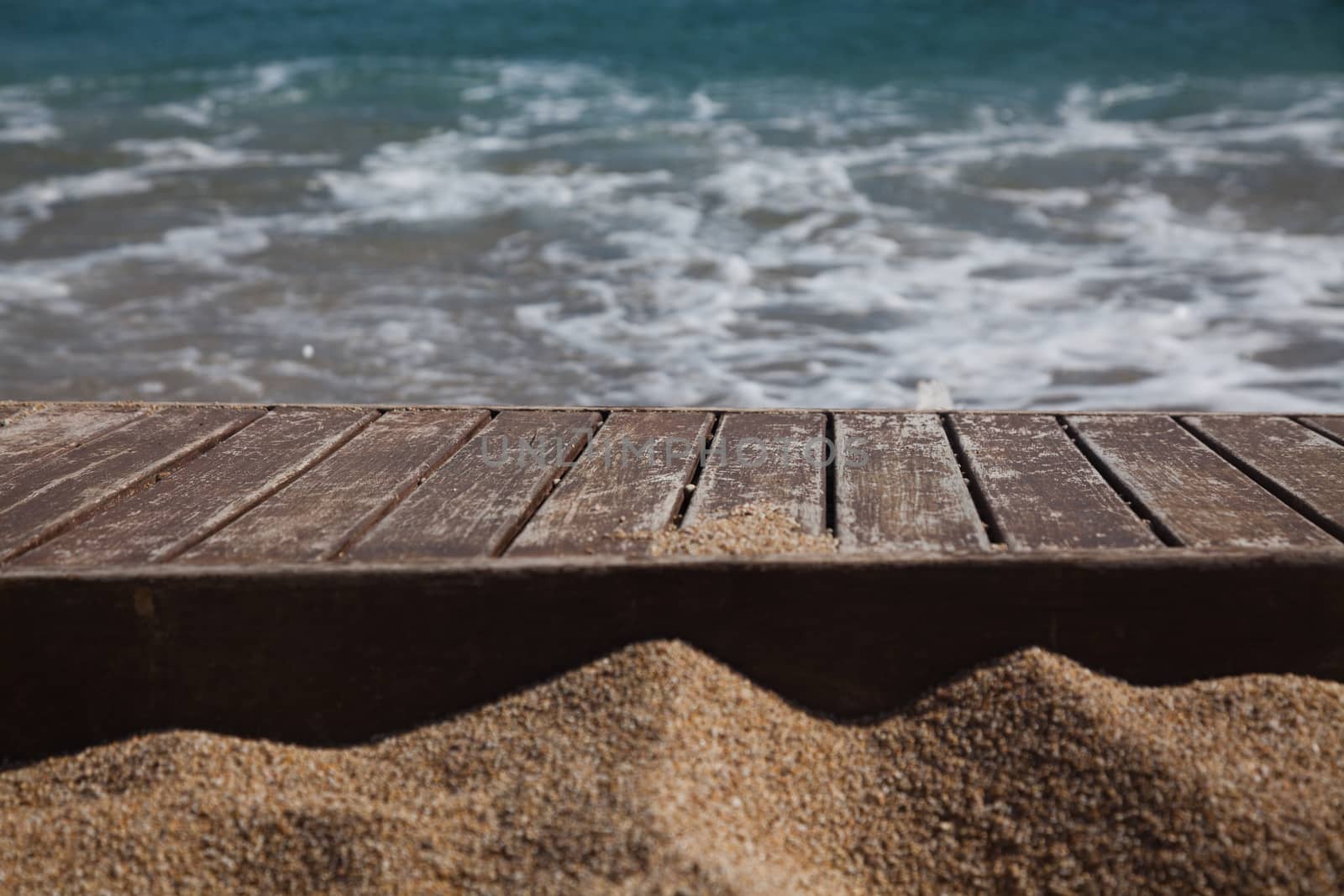 wooden plank in sand and blue sea in the background