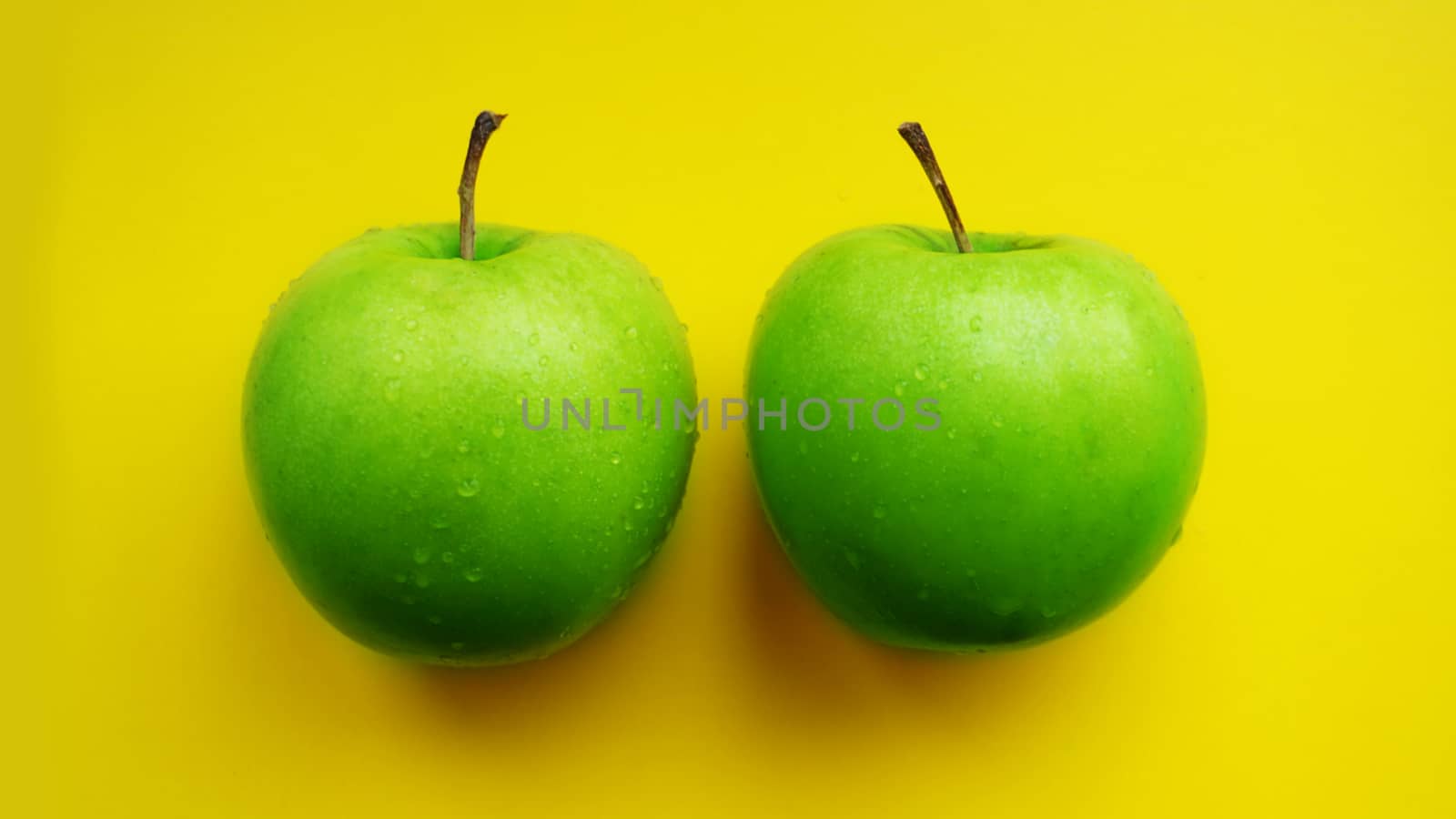 Green apples in water drops on yellow color background isolated close up macro top view