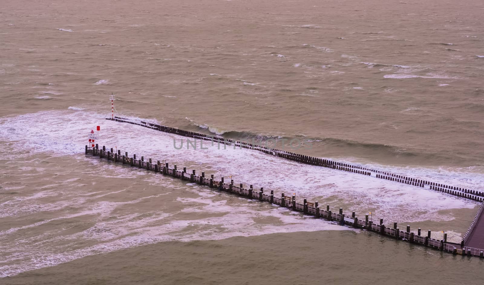 The pier jetty of vlissingen with wooden poles and small lighthouse, wild sea with waves at high tide, Zeeland, The Netherlands