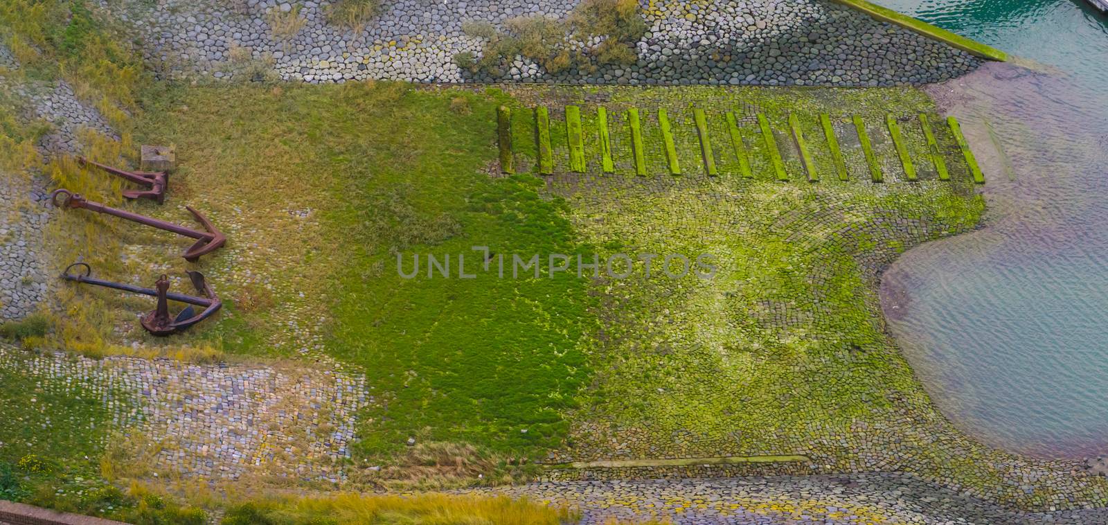 aerial shot of the harbor embankment of Vlissingen, stones covered in green seaweed with ship anchor decorations, dutch landscape