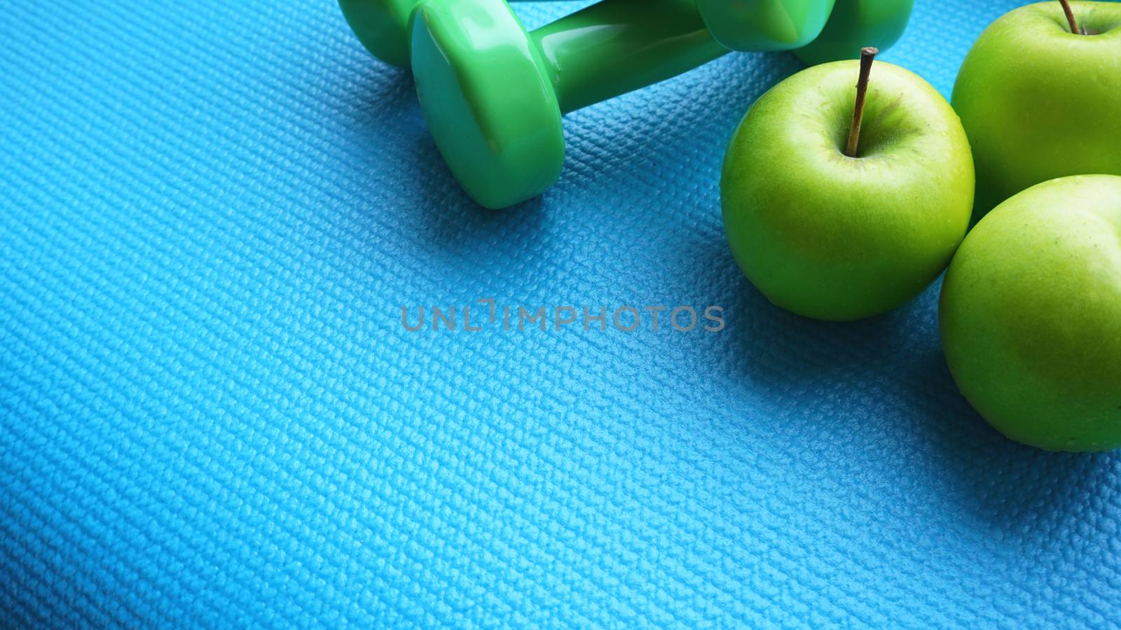 Dumbbells near green apples on blue background. Healthy lifestyle and sports concept. Apple fruit and green barbells. Health regime and fitness symbols