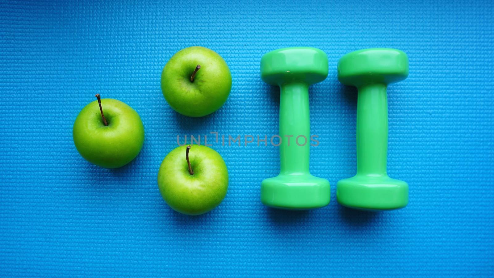 Dumbbells near green apples on blue background. Healthy lifestyle and sports concept. Apple fruit and green barbells. Health regime and fitness symbols