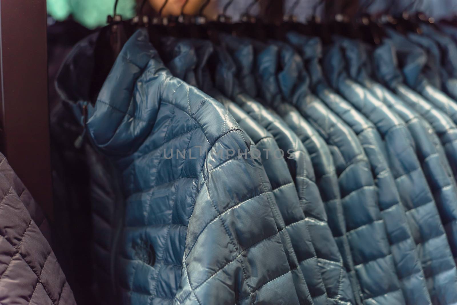 Close-up winter down on clothes rack at American outdoor clothing shop. Insulated fashionable jacket with zip pocket.