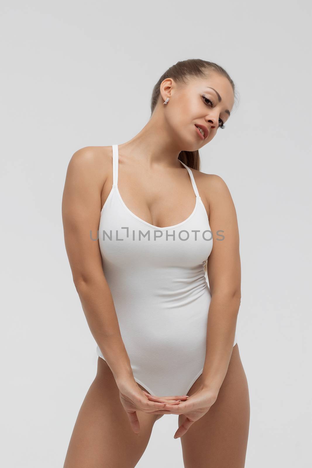 Attractive young woman in white bodysuit looking away in light room