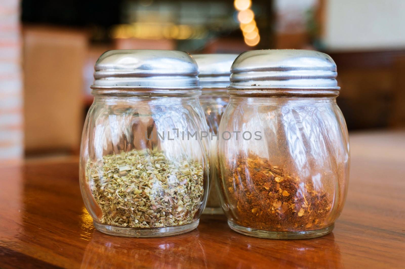 Glass of cheese salt and pepper shakers on wooden table in restaurant.