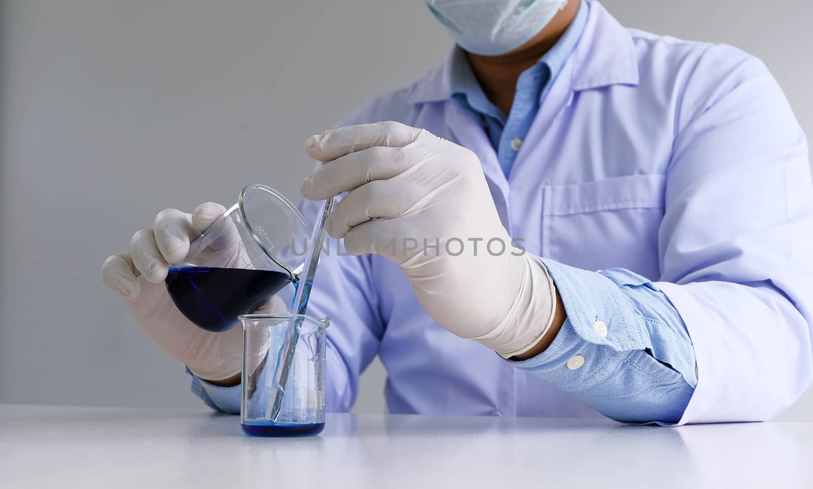 Male medical or scientific laboratory researcher performs tests with blue liquid in lab. Laboratory equipment and science experiments concept