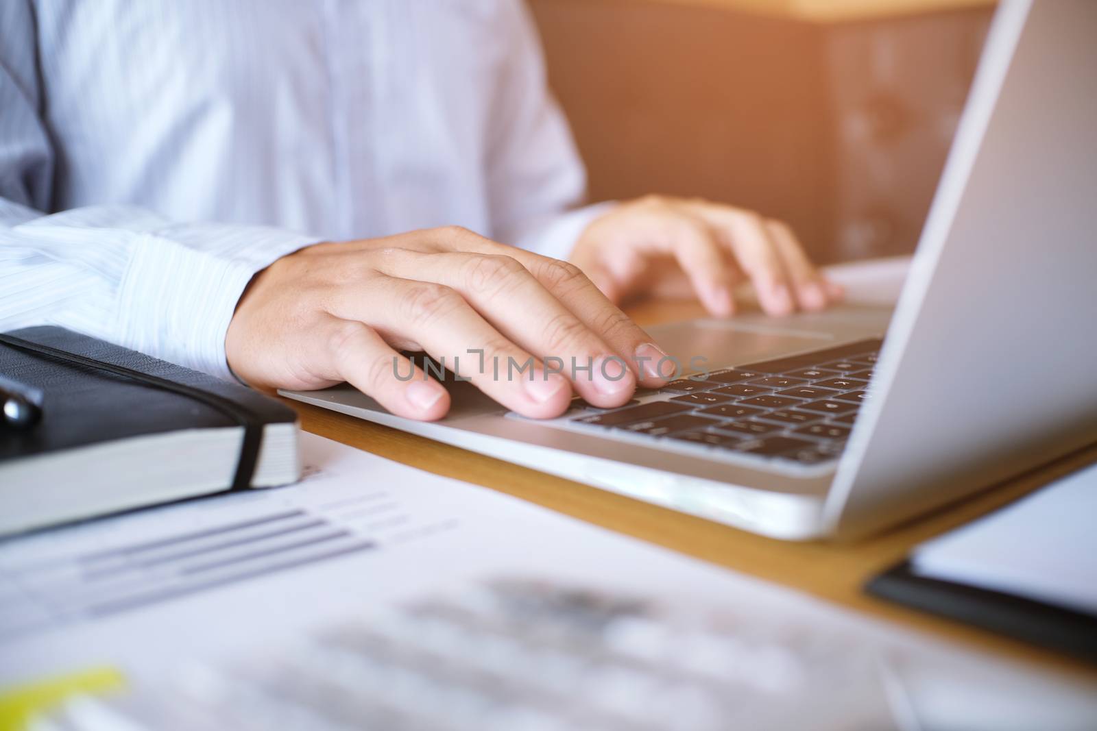 Man working by using a laptop computer on wooden table. Hands ty by peandben