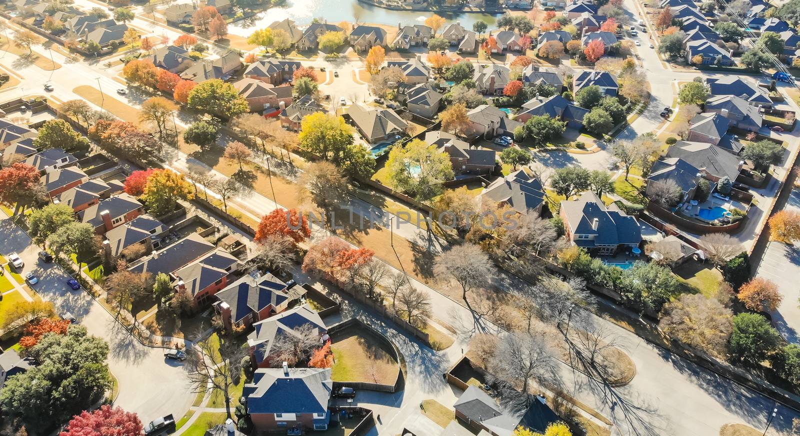 Panorama aerial drone view lakeside residential neighborhood in North of Dallas, Texas, USA during fall season. Row of single-family houses subdivision with colorful autumn leaves
