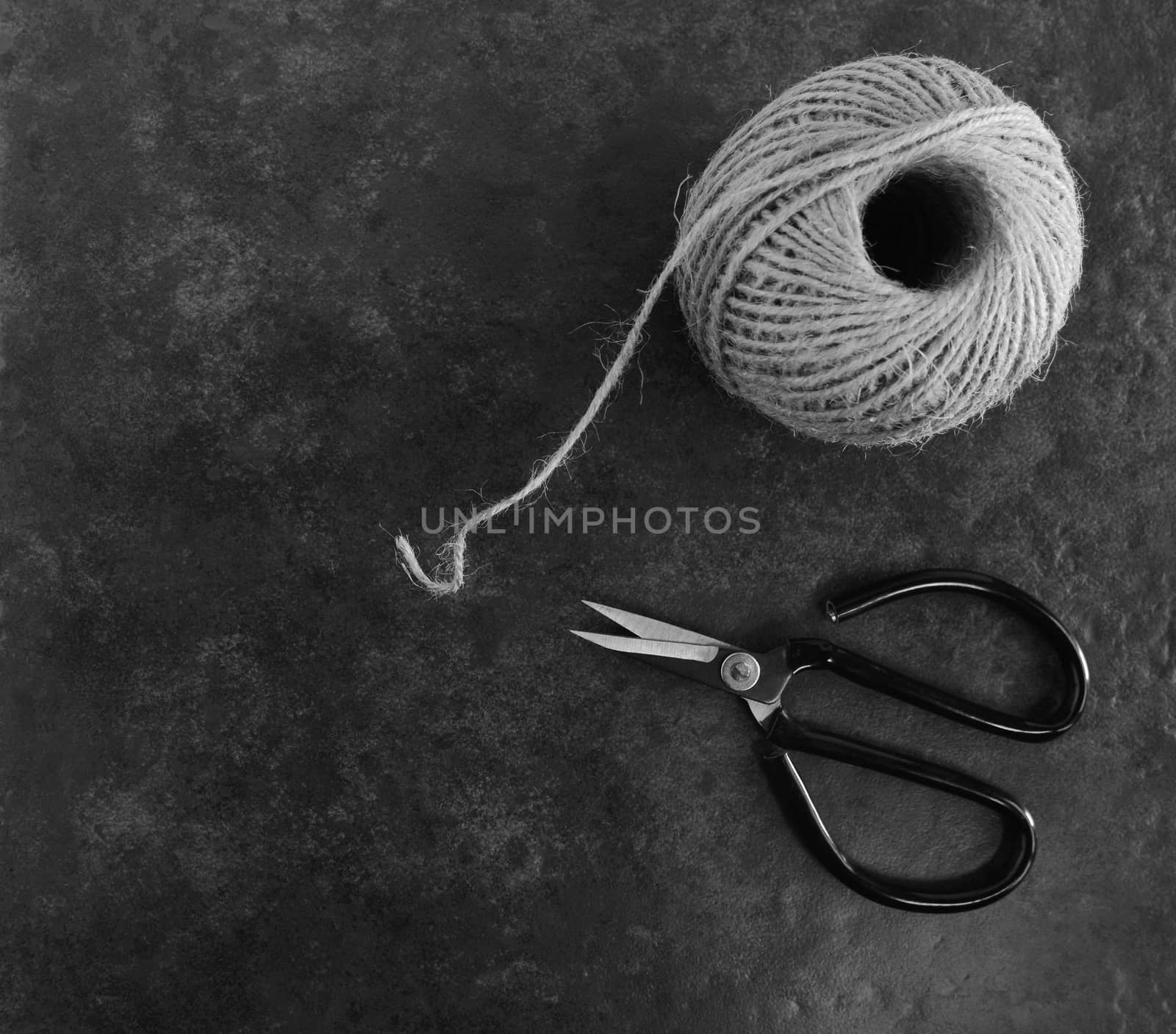 Ball of twine with traditional flower scissors on dark grey background with copy space - monochrome processing