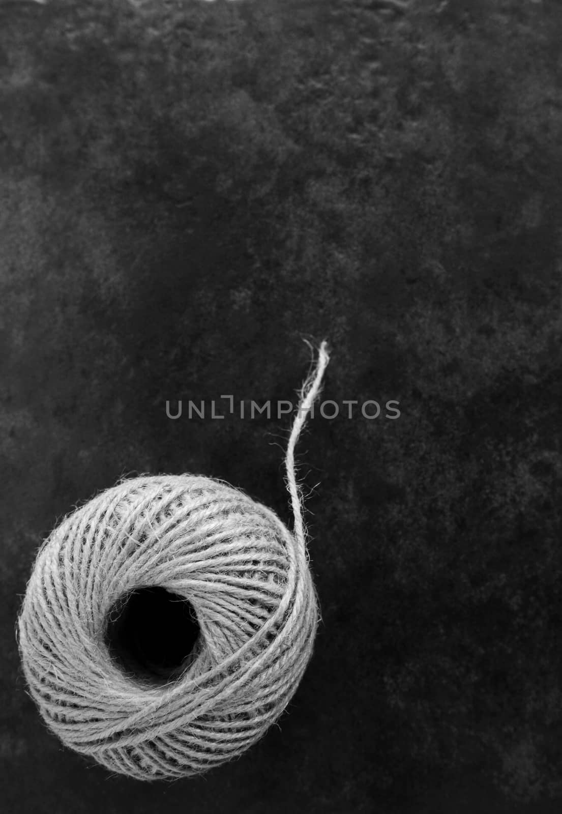Round ball of hessian twine unfurling on a dark grey background with copy space - monochrome processing