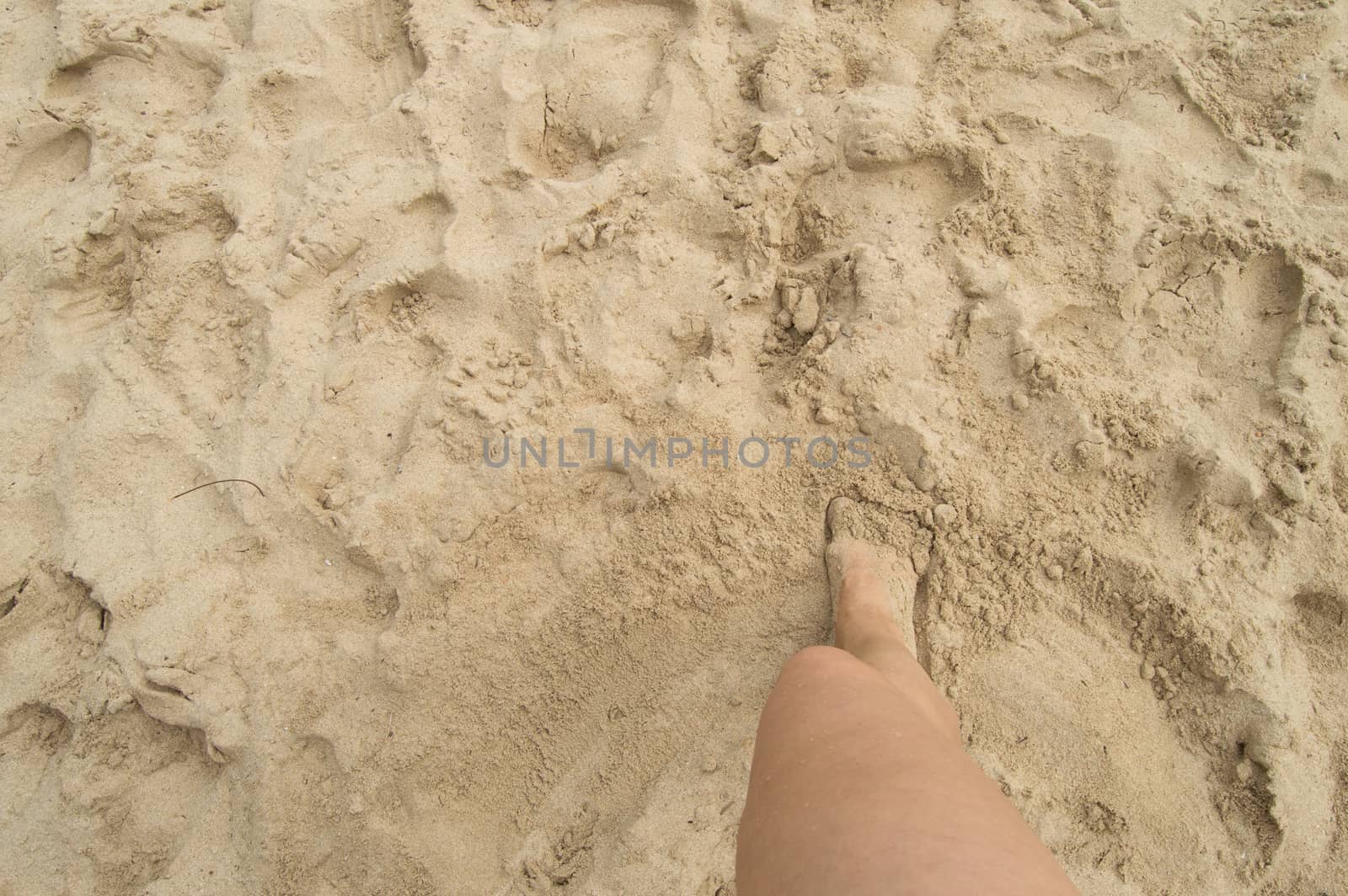 A young woman standing barefoot on the sand on a Sunny summer day. Top view of a beautiful leg. Empty space for text.