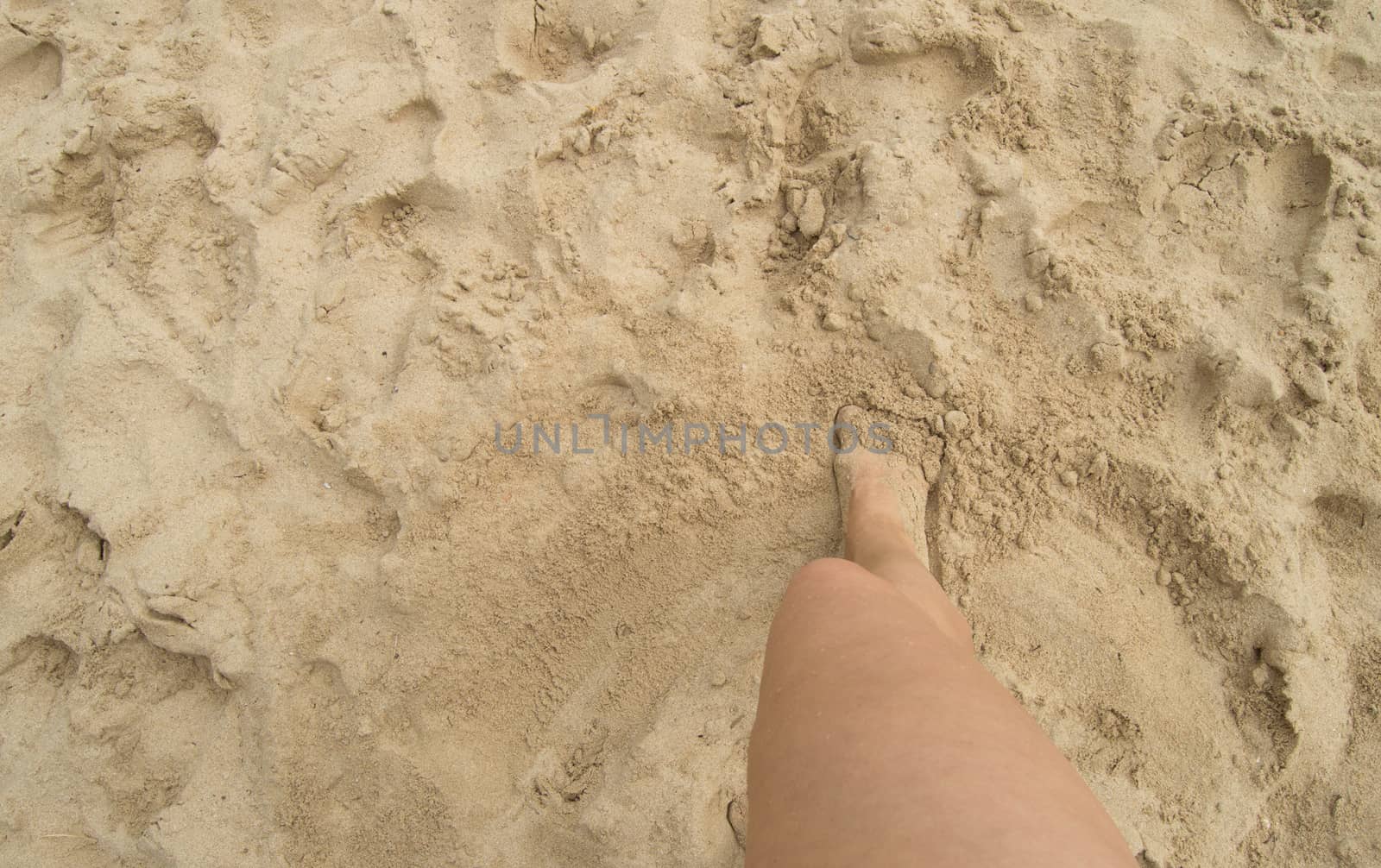 A young woman standing barefoot on the sand on a Sunny summer day. Top view of a beautiful leg. Empty space for text.