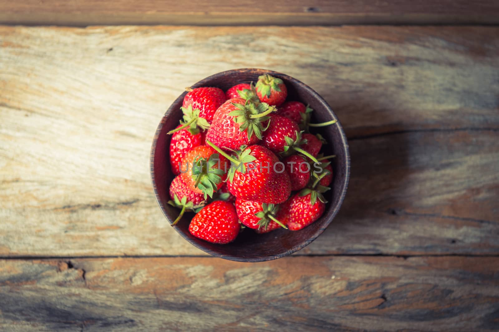 closeup of strawberry fruit in wood cup on grunge wooden background