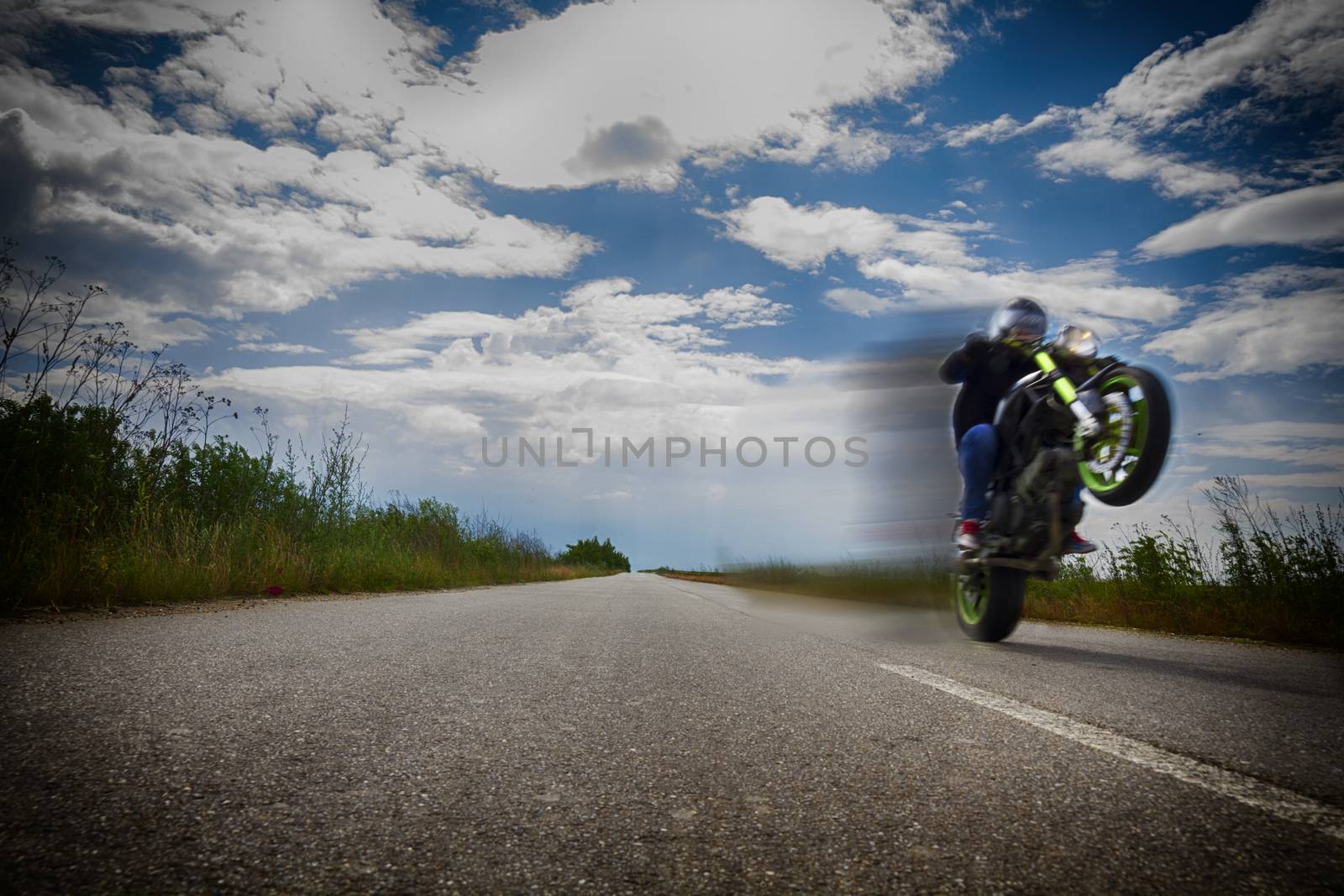 Riding motorcycle on one wheel on empty road and clowdy blue sky