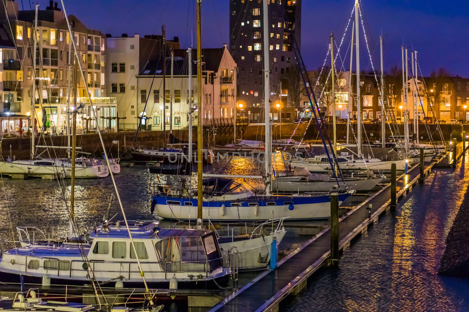 The harbor of vlissingen at night with many docked boats, decorated boats with lights, lighted city buildings with water, popular city in Zeeland, The Netherlands