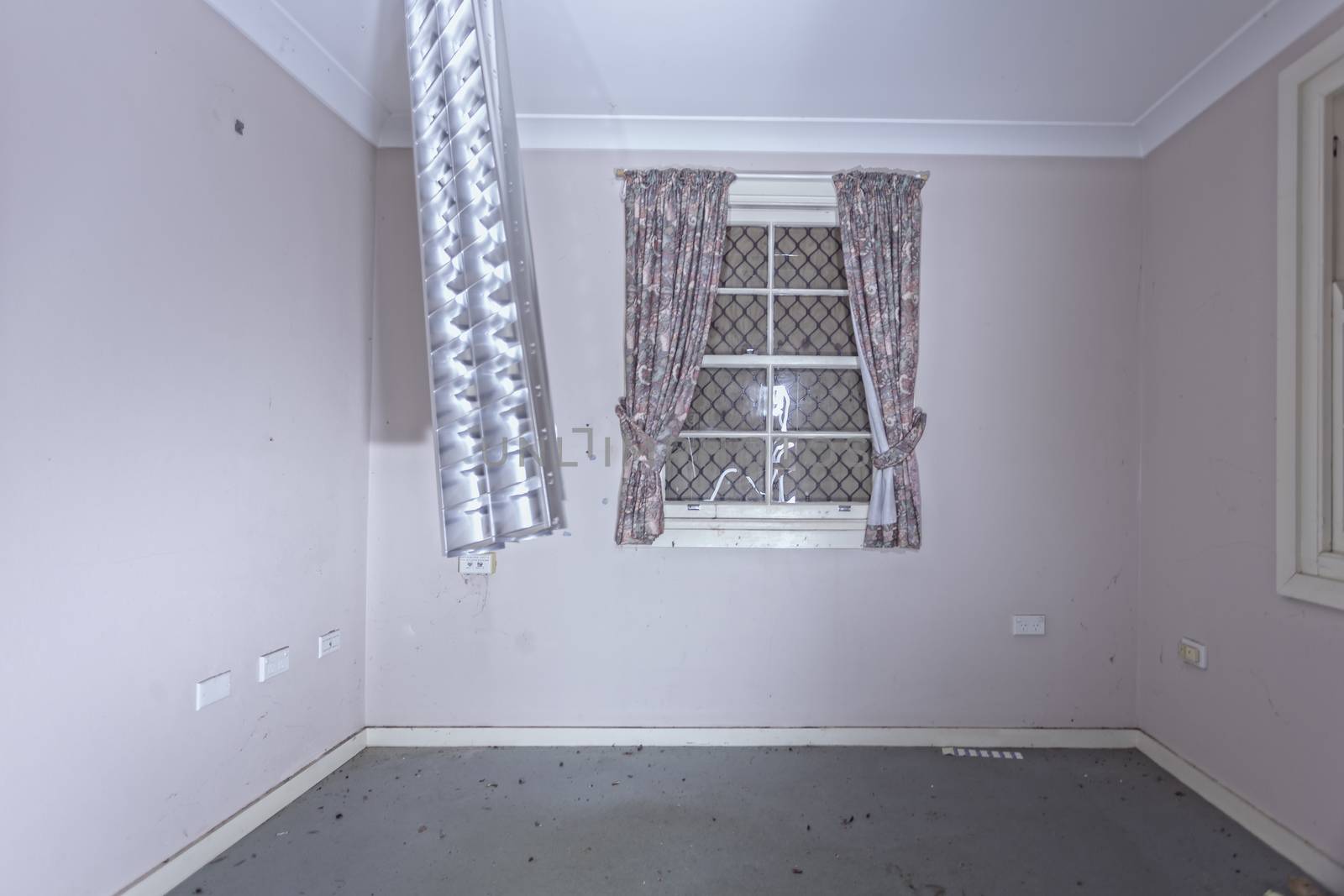 Empty room or office of old abandoned building.  The cover of the fluorescent light fitting is left dangling from the ceiling and the windows have been boarded up