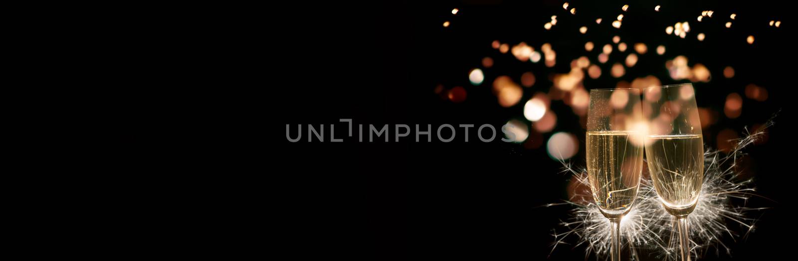 Image of two champagne glasses with burning sparkler on black background