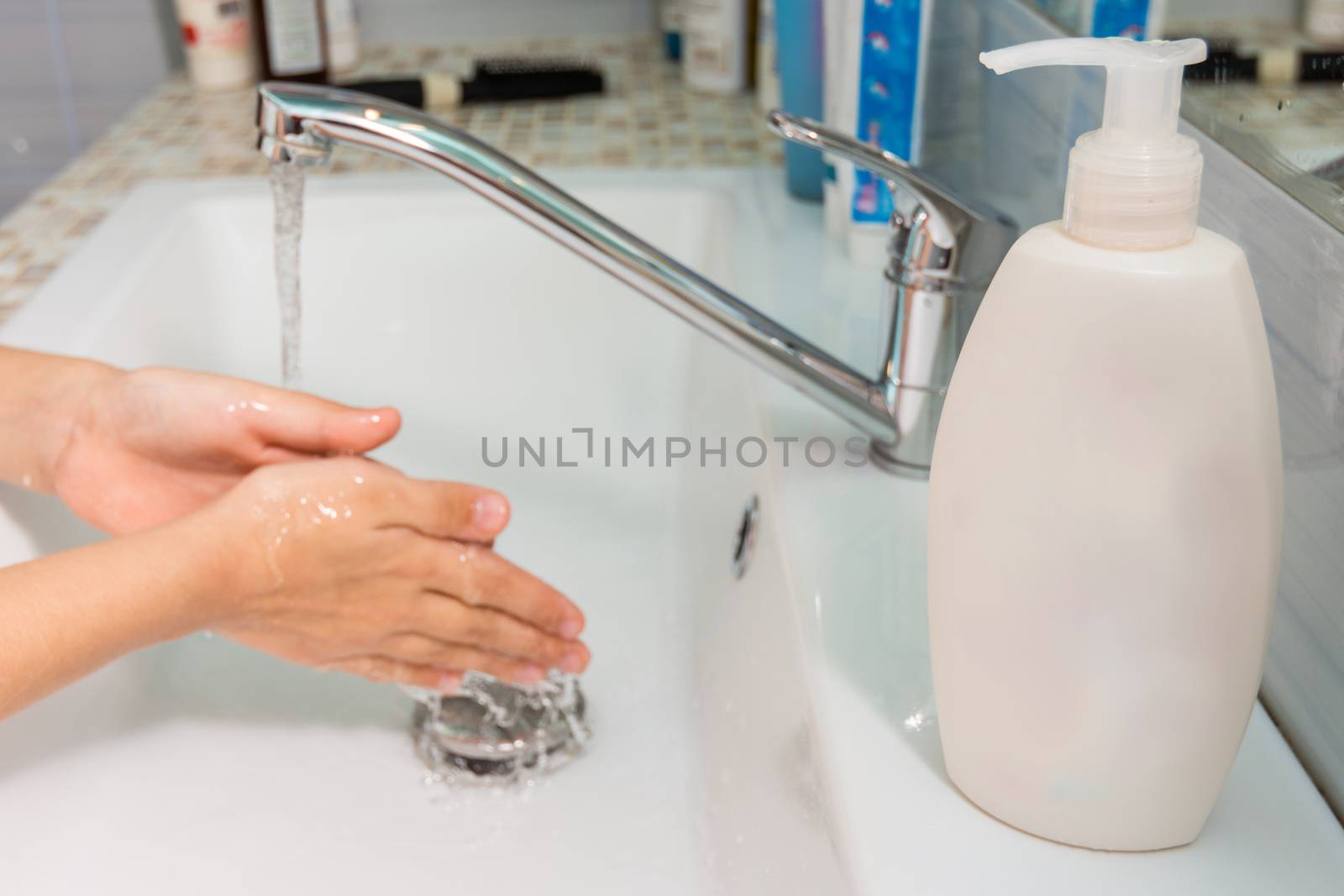 The child washes his hands under the tap, in the foreground a tube of liquid soap