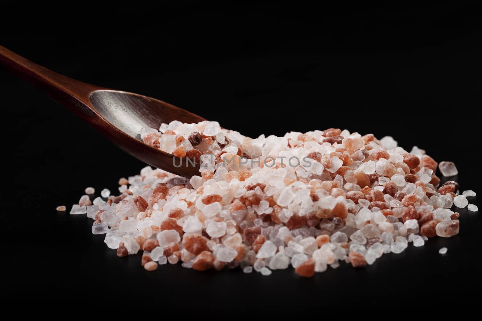 Brown Wood Spoon in Himalayan Salt Pile On Black Background