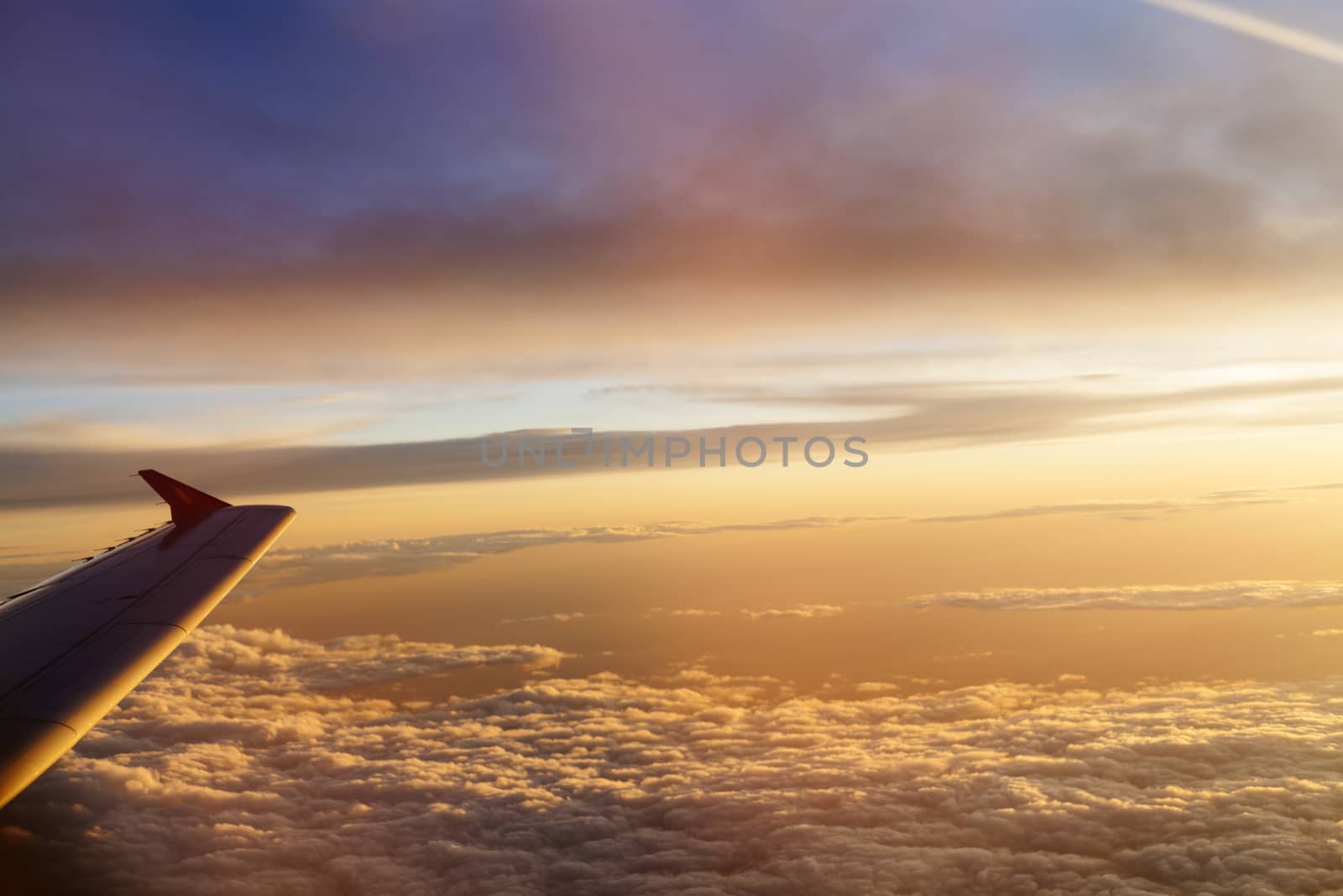 Sunrise over fluffy clouds with airplane wing 