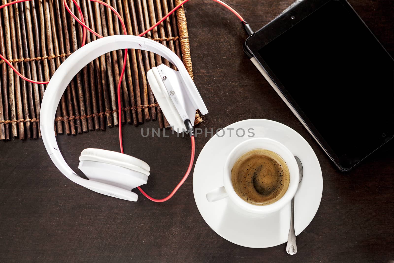 A white cup filled with coffee and headphones on table