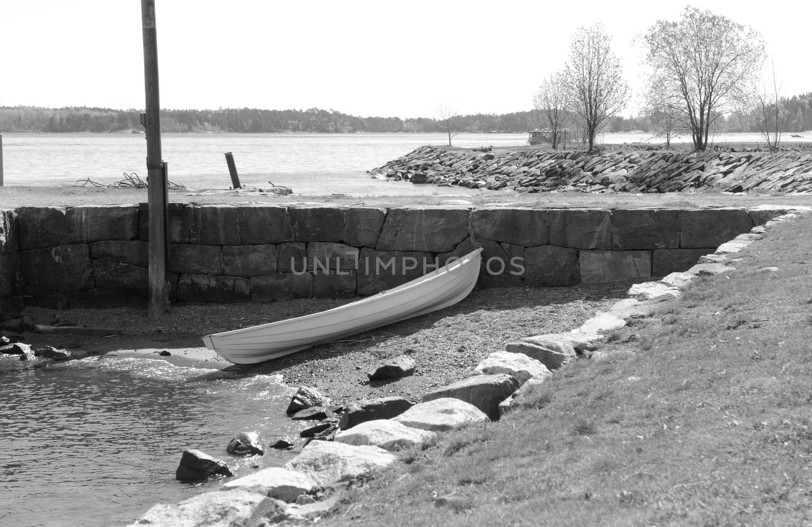 Small white rowboat on a small stony area of shore, against a stone wall on Suomenlinna island, Finland - monochrome processing