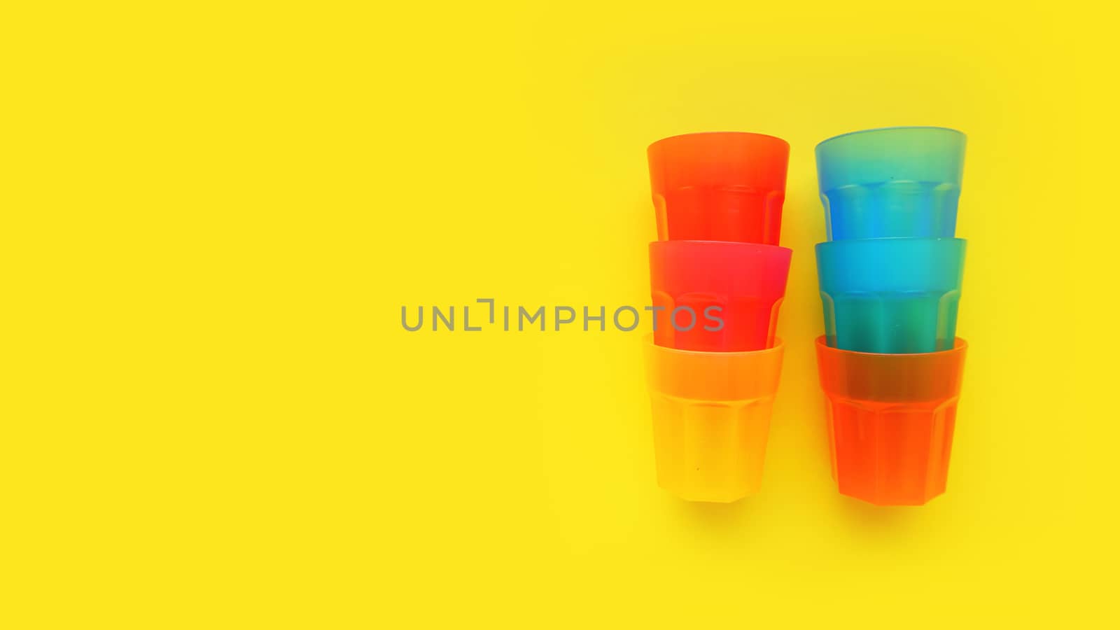 Plastic glass of various color isolated on yellow background - bright summer concept for design and banners