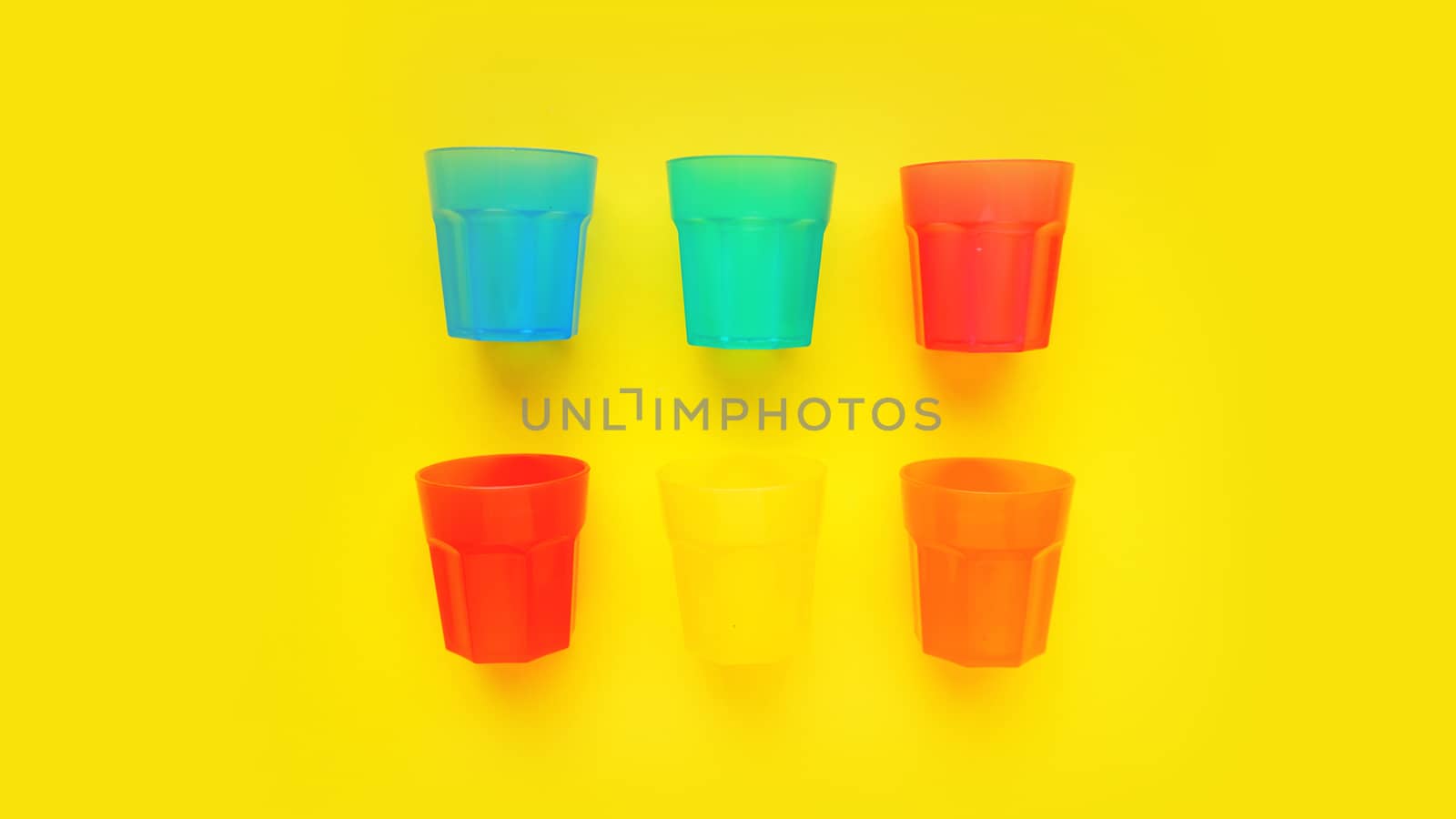 Plastic glass of various color isolated on yellow background by natali_brill