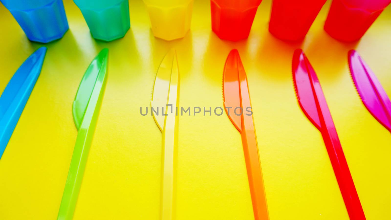 Colored plastic ware. Tableware for a picnic made of colored plastic. Knives and mug in the set of crockery for picnics, tourism and any travel. Yellow background - bright summer concept