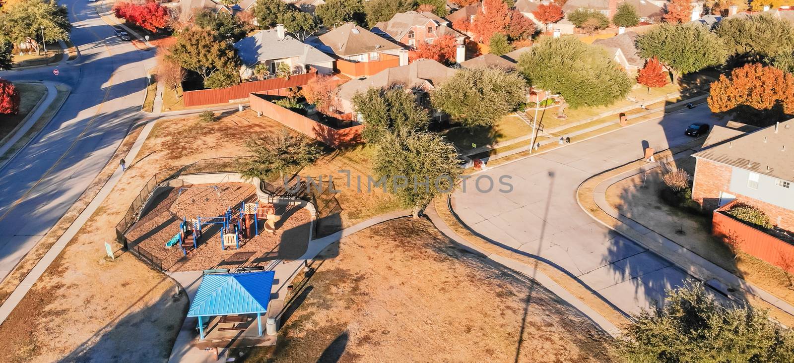 Panorama aerial view of small playground with structure and sand ground in residential area near Dallas, Texas, USA. Single-family houses with bright colorful fall foliage leaves