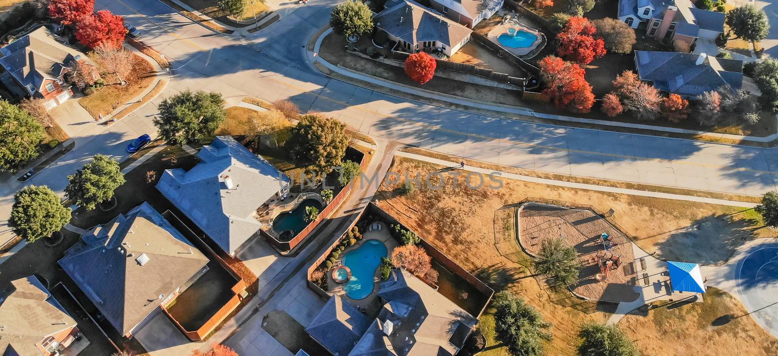 Panorama aerial view of small playground with structure and sand ground in residential area near Dallas, Texas, USA. Single-family houses with bright colorful fall foliage leaves
