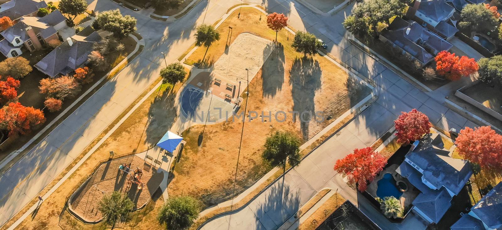 Panorama aerial view of small playground with structure and sand ground in residential area near Dallas, Texas, USA. Single-family houses with bright colorful fall foliage leaves